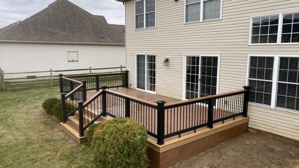 Backyard deck with black railing behind a two-story home