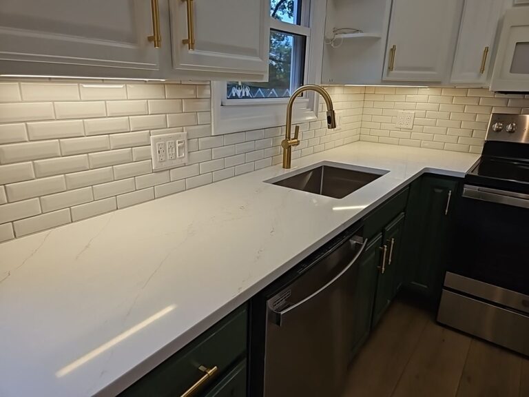 White subway tile backsplash around a kitchen window above white counters and dark green lower cabinets