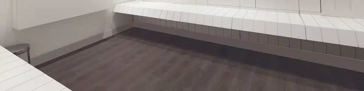Daltile Elixen Black Walnut wood-look luxury vinyl floor below white built-in bench seating in a manufacturer interior scene