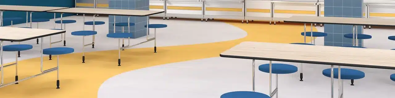 Daltile Loften fabric-look luxury vinyl flooring with pale gray fields and a yellow curved accent beneath cafeteria tables in a manufacturer scene