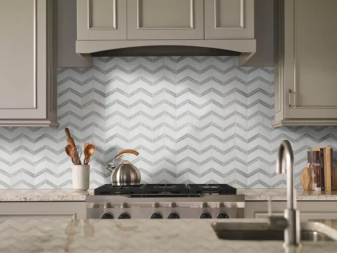 MSI Bianco Dolomite polished marble chevron backsplash behind a stainless range beneath gray cabinets in a manufacturer scene