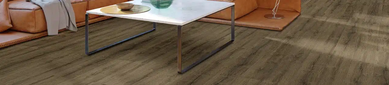 MSI Kallum wood-look luxury vinyl floor beneath a coffee table and beside a tan leather sofa in a manufacturer living room scene
