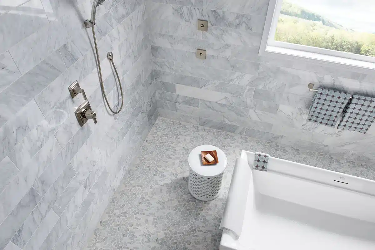 MSI Rio Lago Sliced Carrara White marble pebble floor beside a bathtub and shower fixtures in a manufacturer bathroom scene